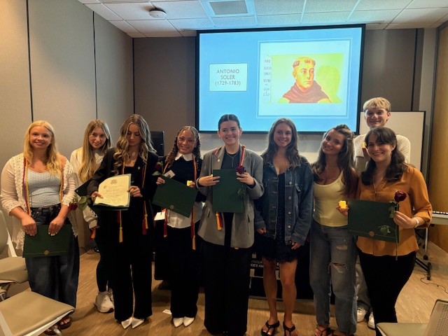 Students at sigma delta pi ceremony holding certificates and graduation cords
